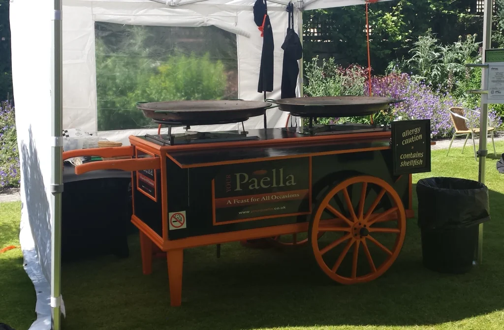 Traditional Your Paella catering cart fully set up with two large paella pans ready for live cooking at a private event.