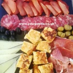 a mixed spanish meat and cheese platter with tortilla chunks and olives