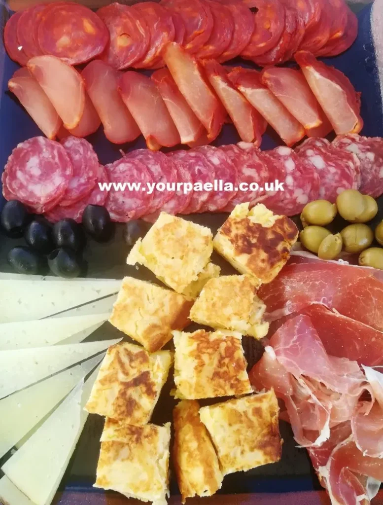 a mixed spanish meat and cheese platter with tortilla chunks and olives