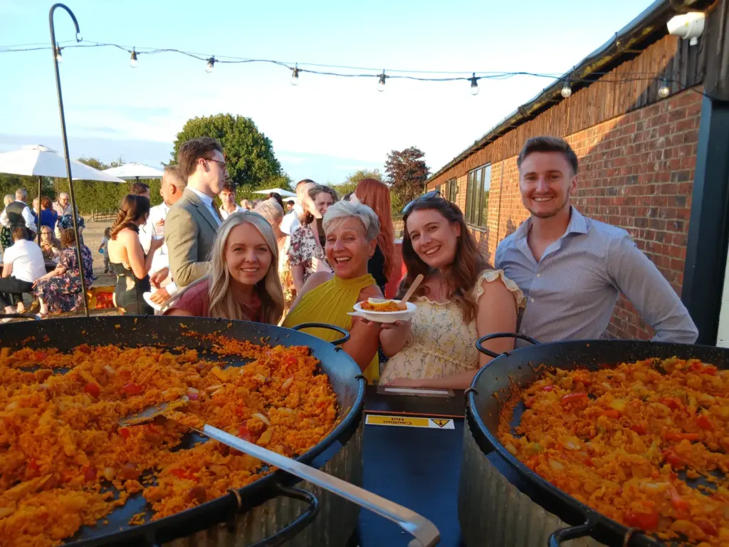 Guests enjoying freshly cooked chicken, chorizo and vegetarian paella at an outdoor wedding reception at The Tractor Barn, Stone Siding Events, Northamptonshire.