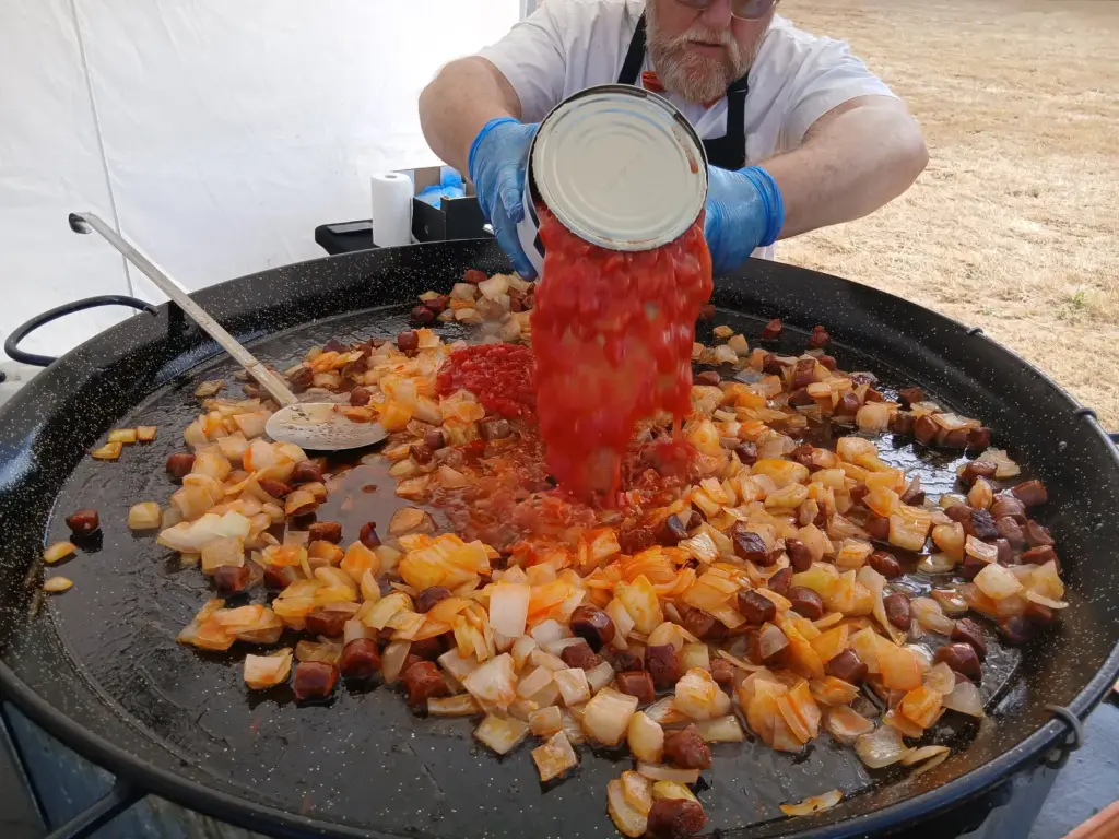 Chopped tomatoes being added to a large paella pan