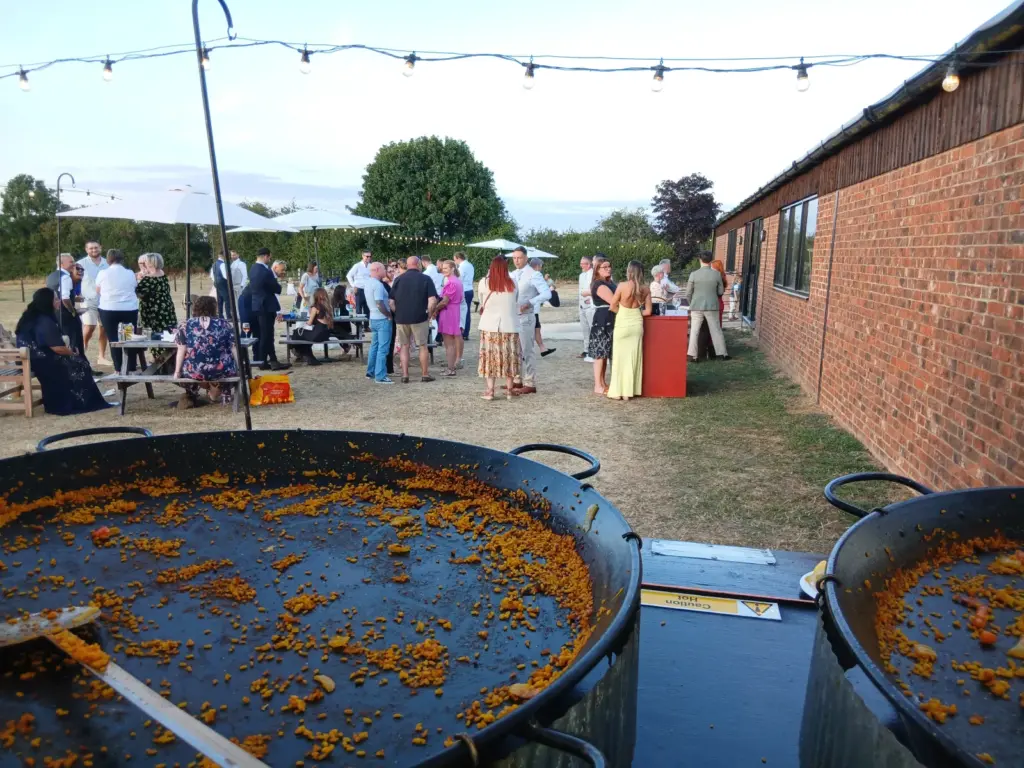 Guests enjoying an outdoor wedding reception at The Tractor Barn, Stone Siding Events, Northamptonshire after freshly cooked paella was served.